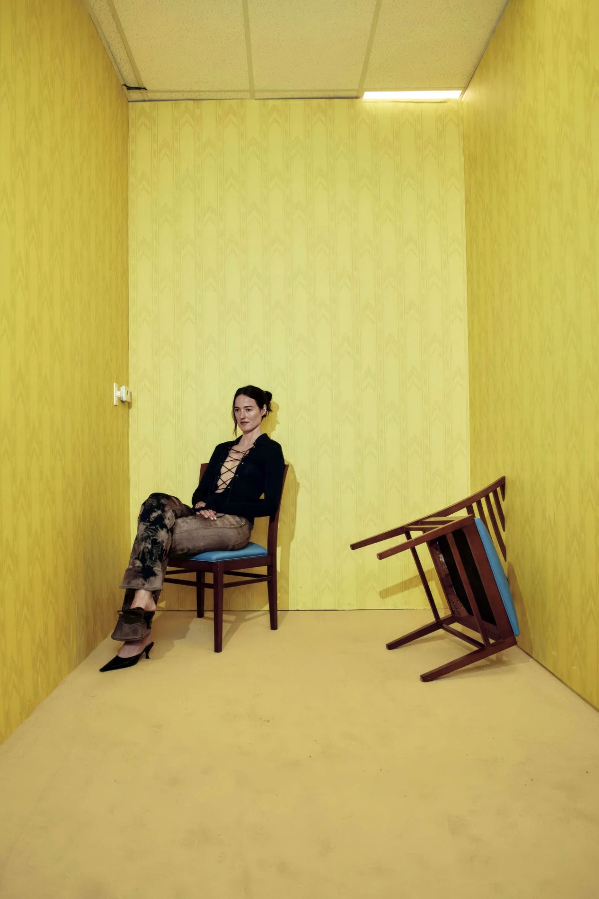 Backrooms poster showing a woman seated in a yellow room beside an overturned chair