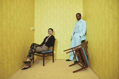 Backrooms Yellow Room Duo poster with a seated woman, standing man in pale blue, and overturned chair