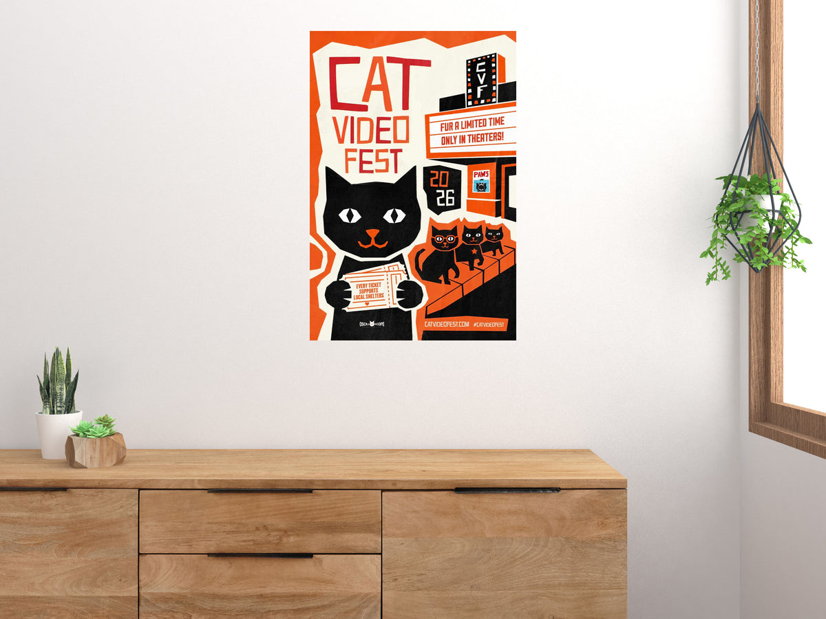 Cat Video Fest poster displayed above a wooden sideboard in a bright room with houseplants