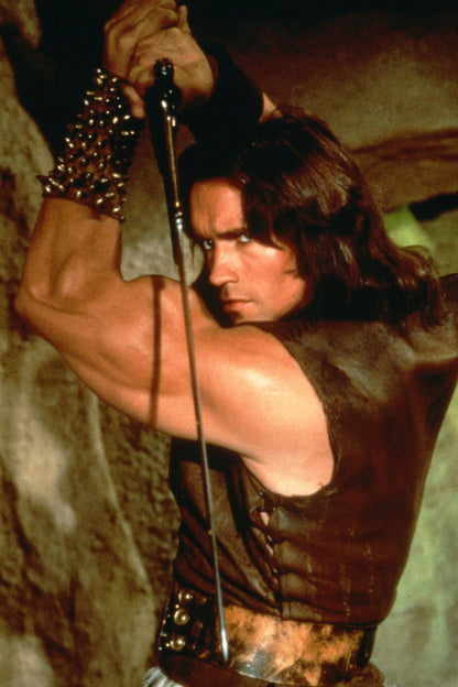 Conan fantasy movie character poster showing a warrior holding a raised sword in warm brown and gold tones