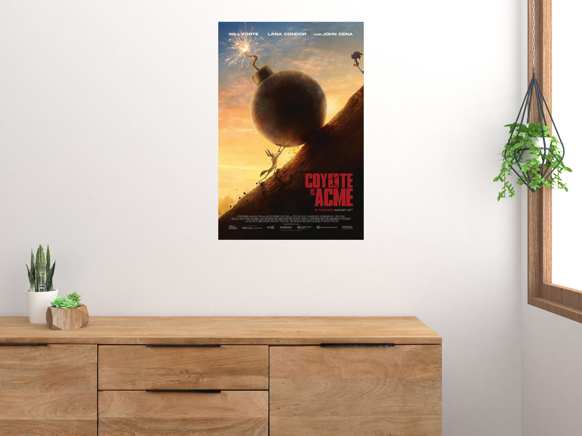 Coyote vs. Acme poster displayed above a wooden sideboard beside a window and houseplants