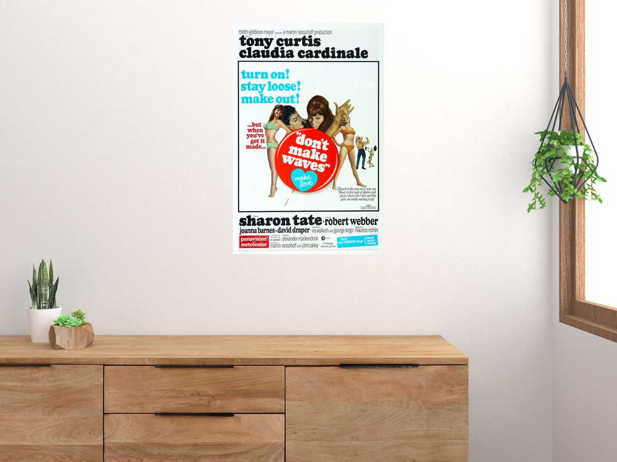 Don't Make Waves movie poster displayed above a wooden sideboard beside houseplants and a window