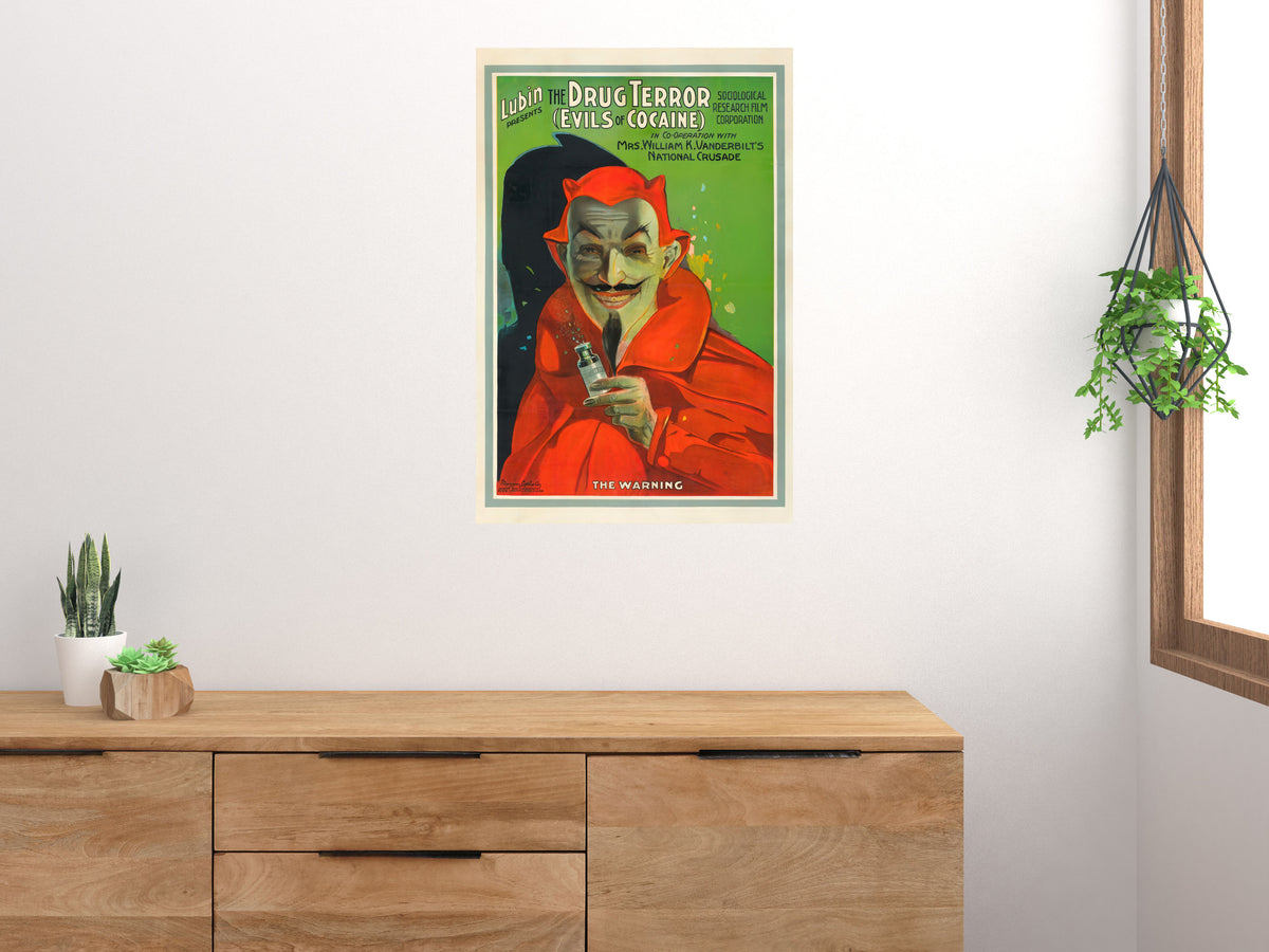 The Drug Terror red devil movie poster displayed above a wooden sideboard beside a window and plants