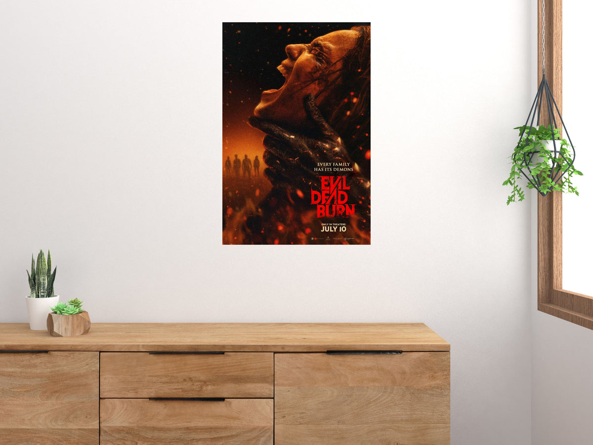Evil Dead Burn vertical horror movie poster displayed on a light wall above a wooden cabinet